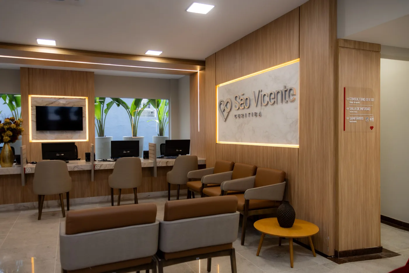 Sala de espera com poltronas, televisão e balcão de recepção